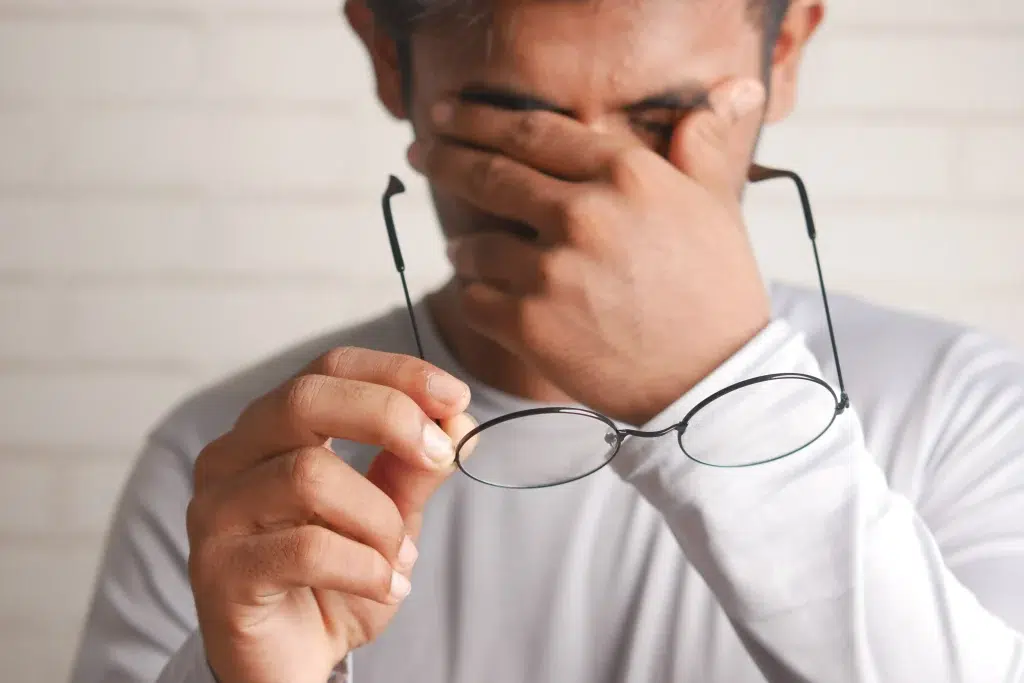 A guy is holding his glasses, seemingly in pain
