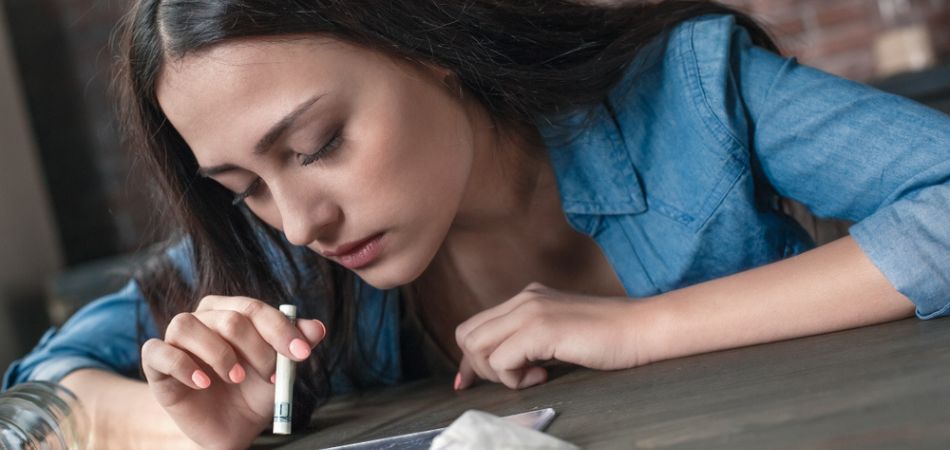 young woman inhealing cocaine on table